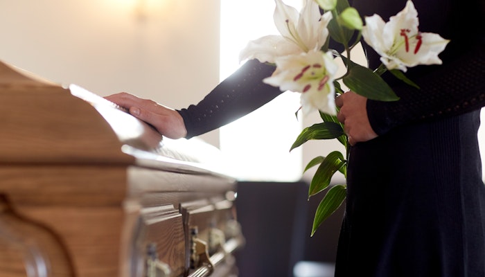 woman touching casket with flowers in other hand