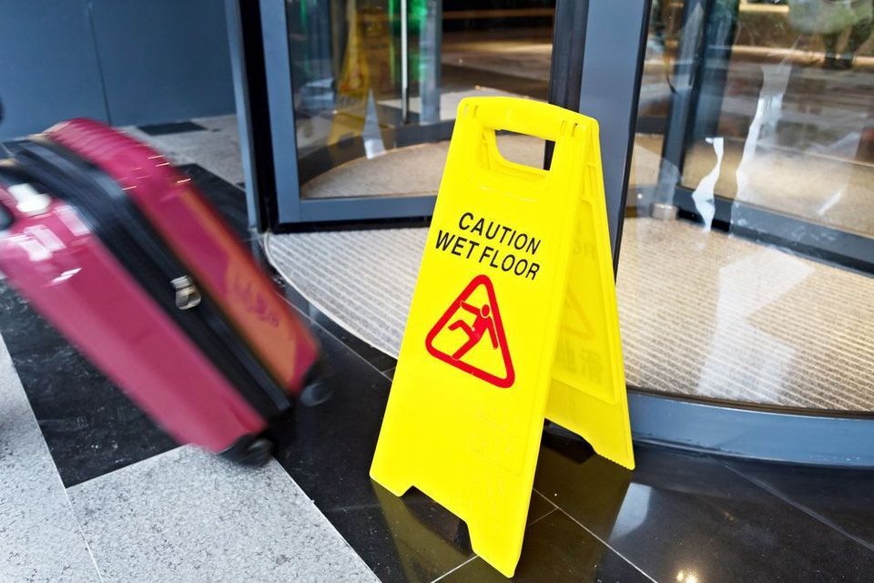 Caution slipper floor sign next to rolling suitcase and revolving door