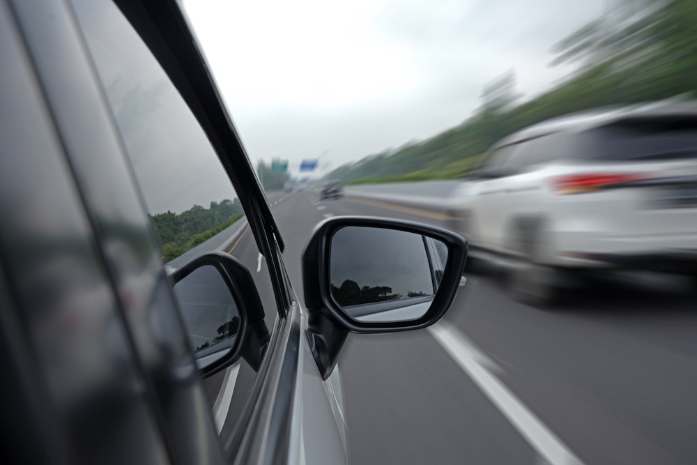 Close-up of a car's side mirror while speeding on a highway