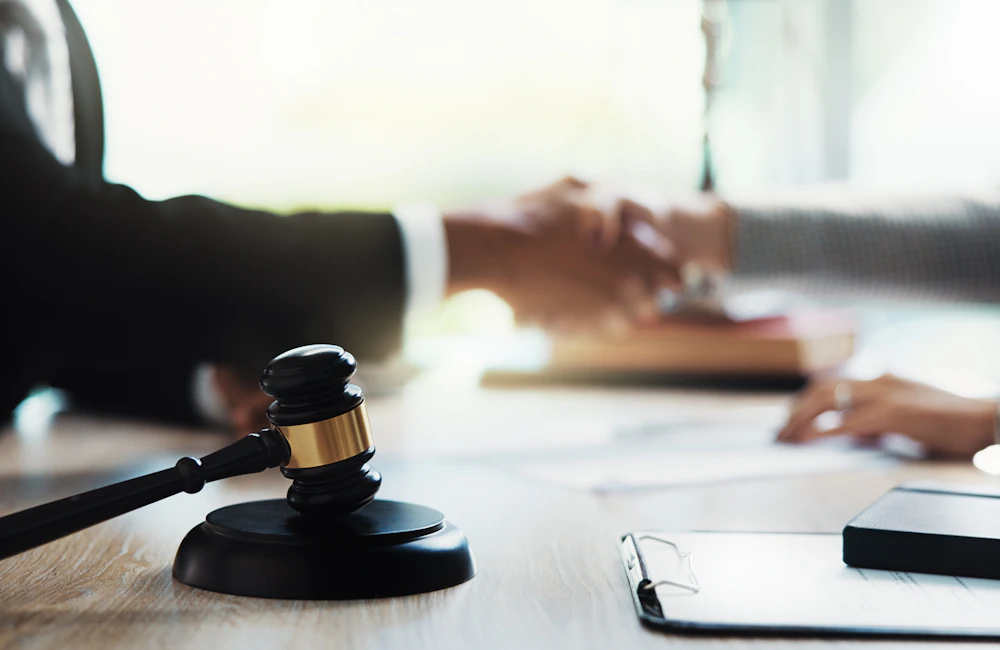 Lawyer and client shaking hands with gavel in the foreground