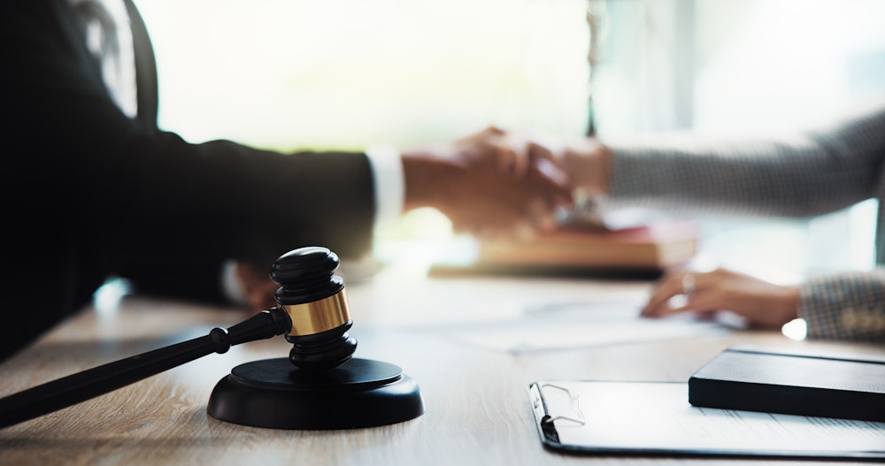 Lawyer and client shaking hands with gavel in the foreground