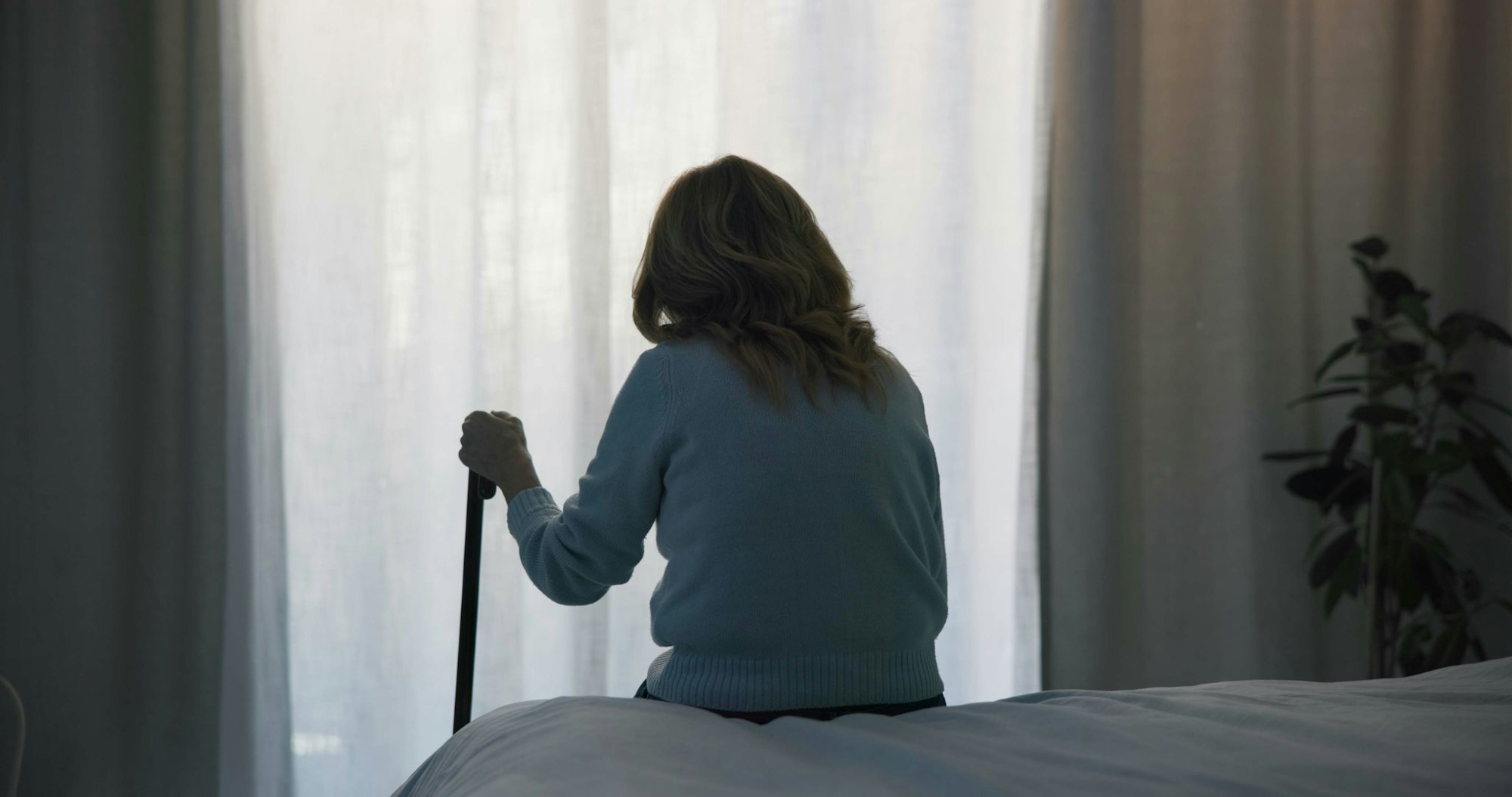 Elderly woman with cane sitting on a bed