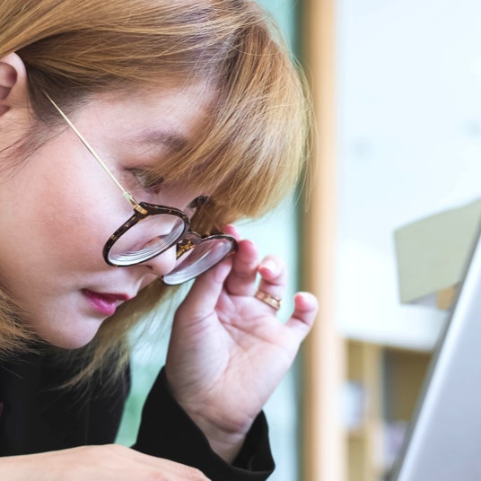 woman lowering glasses, squinting, and leaning in to see a computer screen