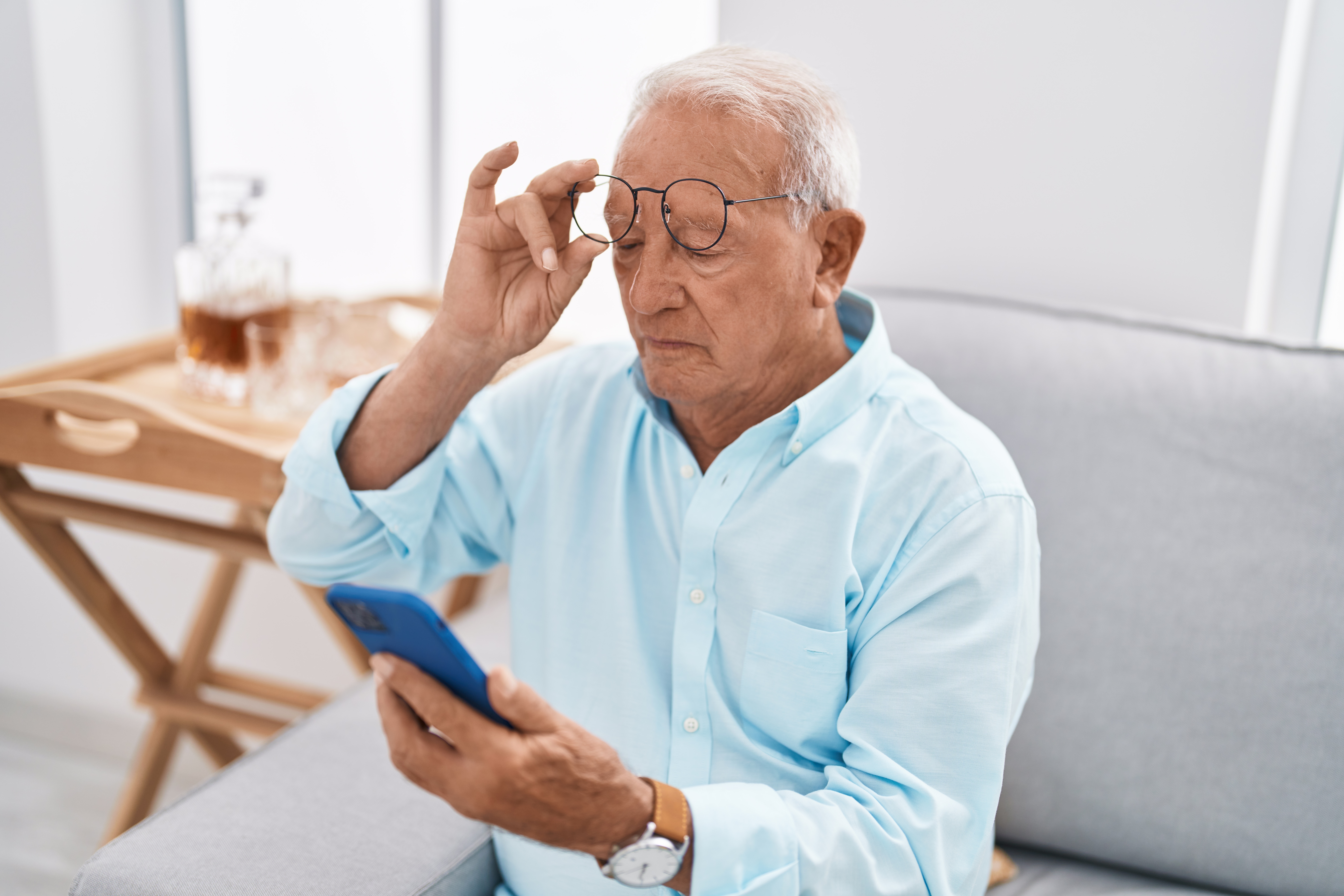 Mature man removing glasses while trying to read phone