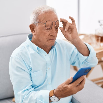 Mature man removing glasses while trying to read phone