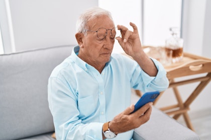 Mature man removing glasses while trying to read phone