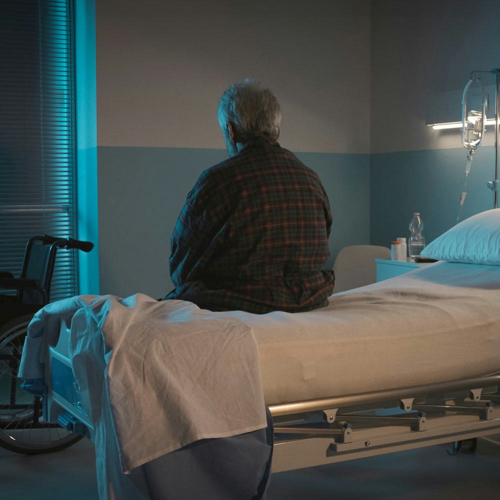 Back of elderly man sitting on a hospital bed
