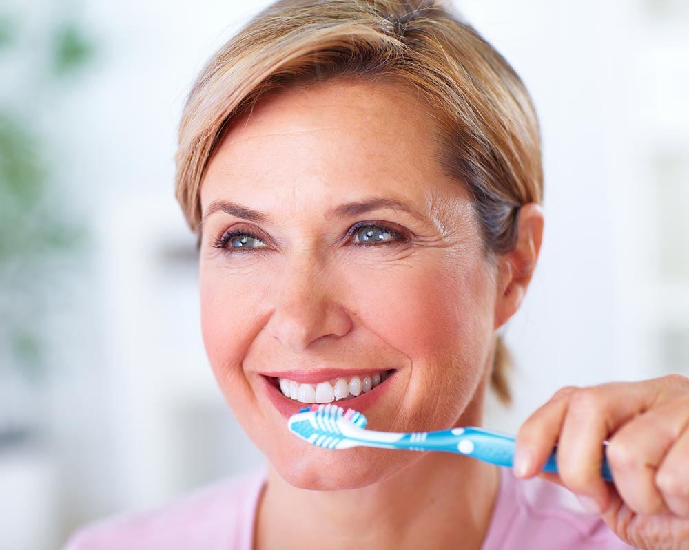 Smiling mature woman brushing teeth