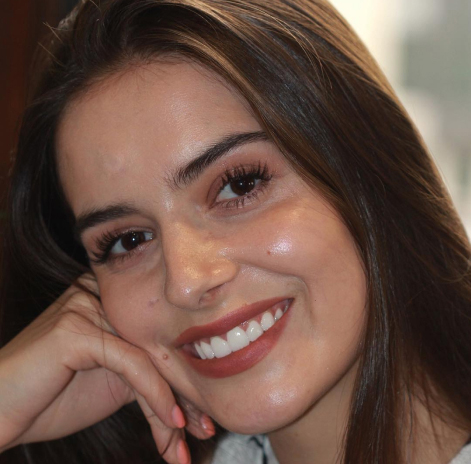 Smiling young woman with long dark hair resting her chin on her hand in a close-up portrait