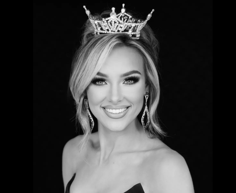 Miss South Carolina 2023 holding flowers and a trophy plate, smiling on stage with one arm raised
