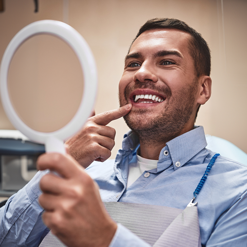 man admiring his smile in a handheld mirror