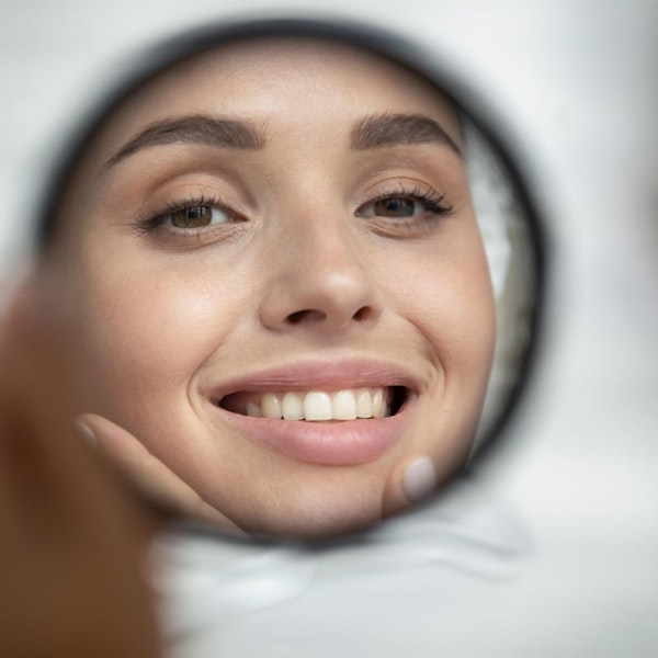 woman with dental implants smiling in hand mirror