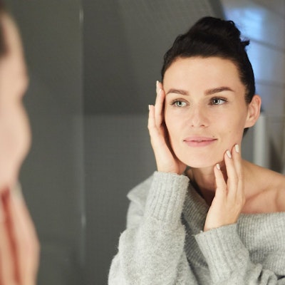 Woman looking at reflection in mirror with hands on face