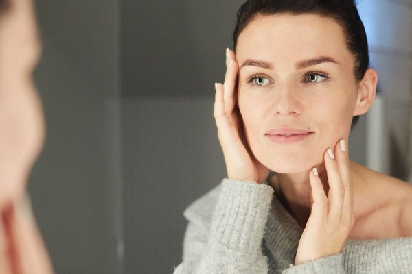Woman looking at reflection in mirror with hands on face