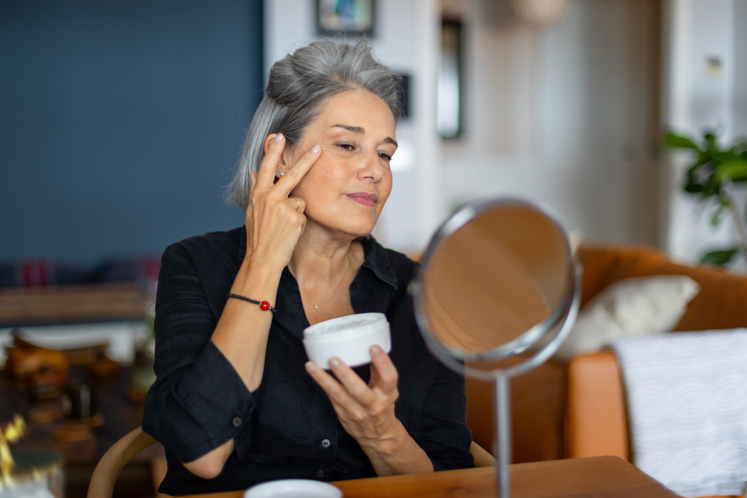 woman putting on moisturizer in small mirror