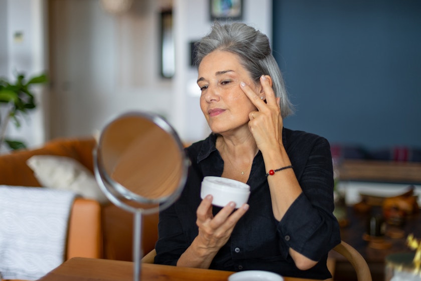 woman putting on moisturizer in small mirror