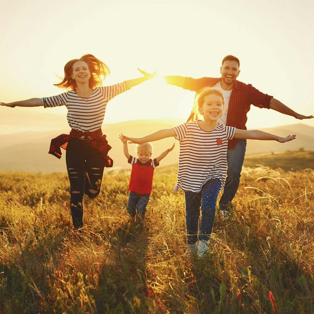 A young family of four running towards the camera while the sun sets in the distance