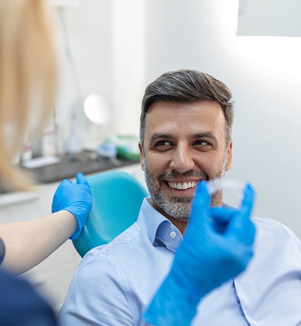 Smiling man in dental chair discussing Invisalign with dentist