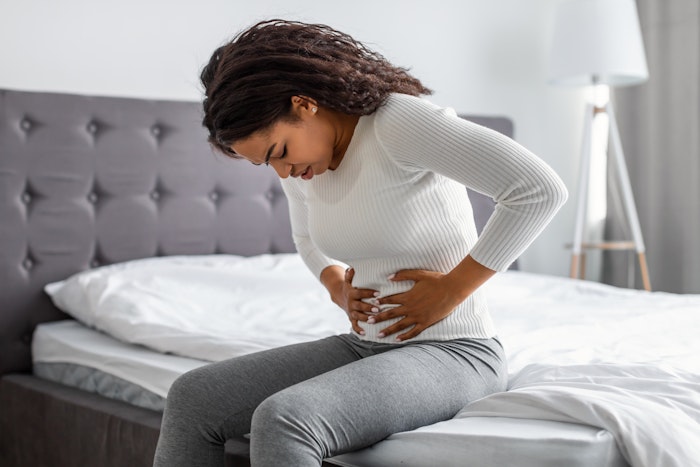 Woman sitting on bed clutching stomach