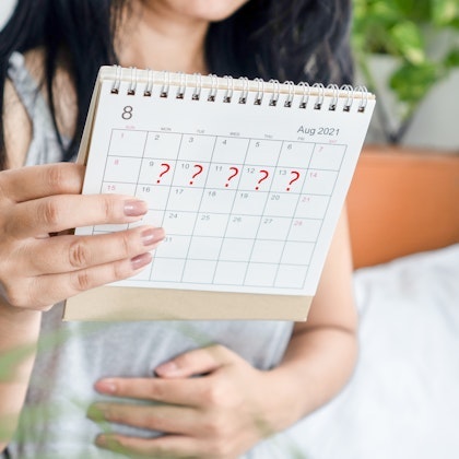 Woman holding a calendar with question marks while holding her stomach