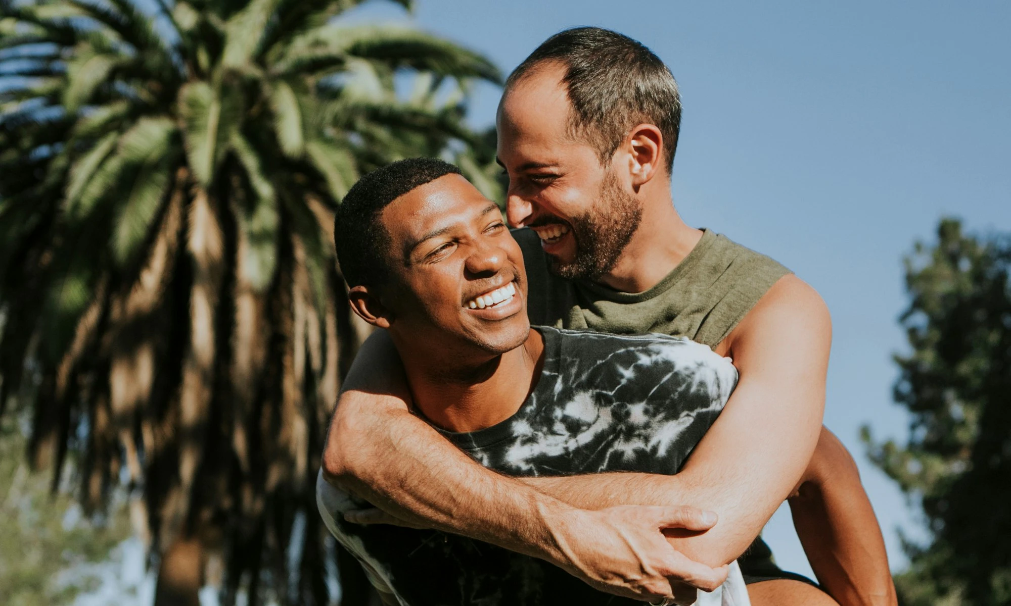 Two men smiling and embracing outdoors near palm trees