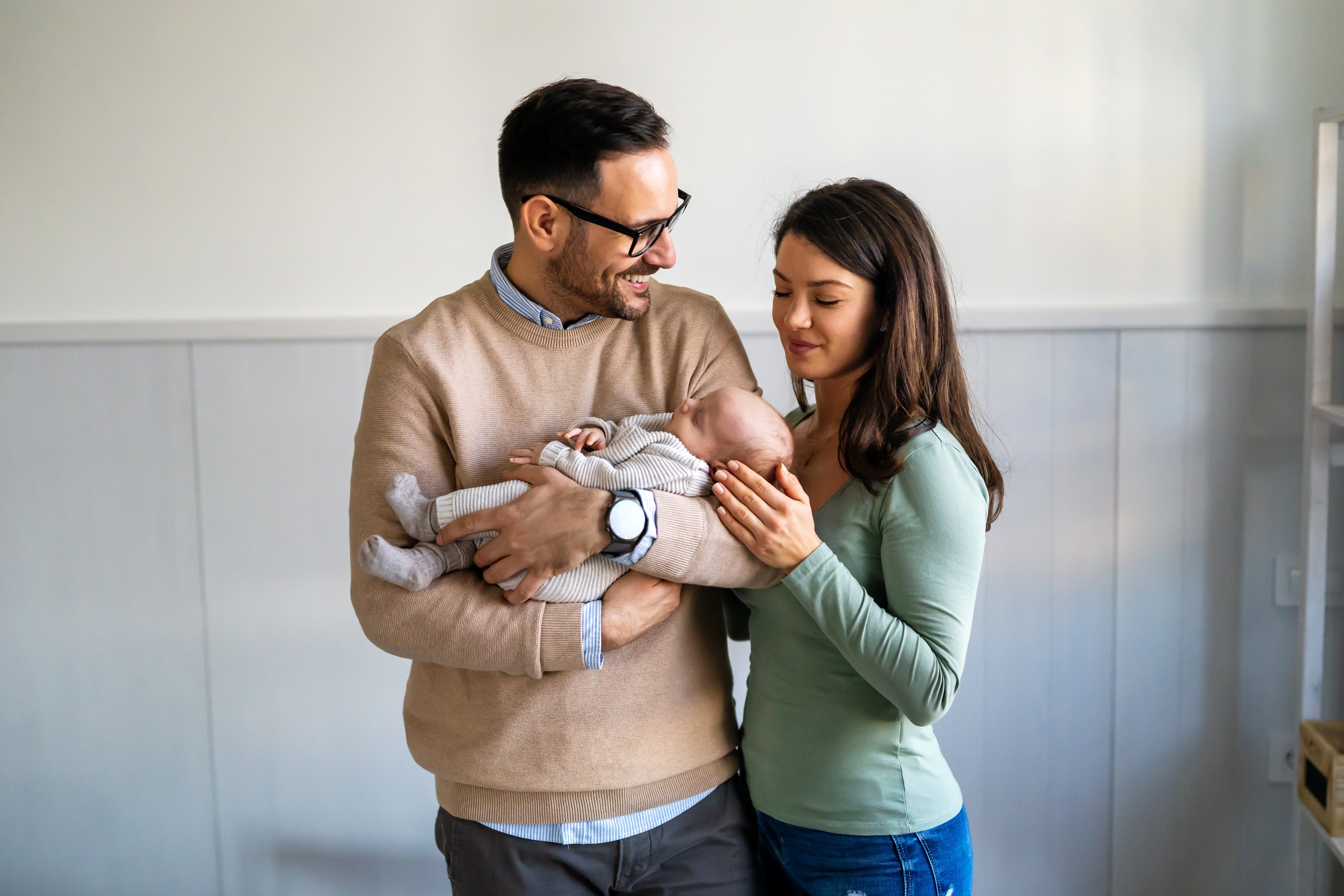 Man in glasses and woman in green top looking down at a newborn baby they are holding together