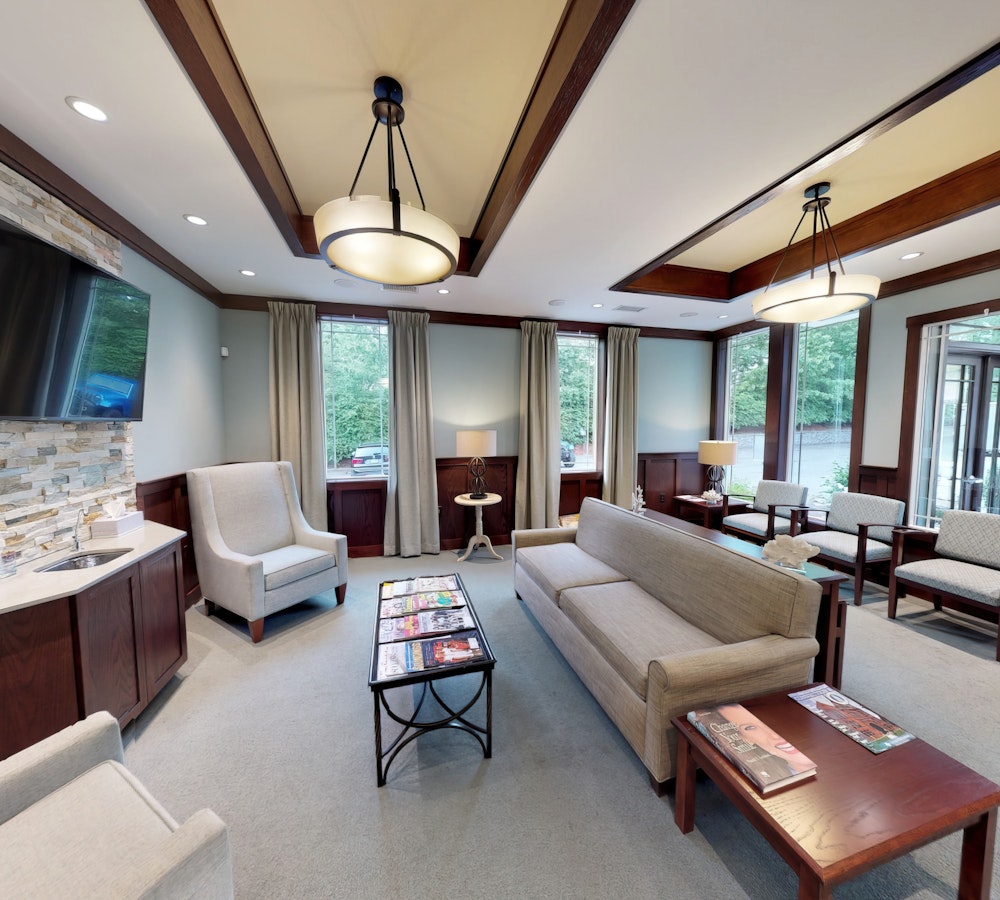 Reception area at Drs. Hadden & Whidden, LLC featuring neutral-toned seating, modern lighting, and large windows overlooking wooded surroundings