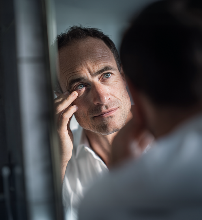 Un homme se touchant l'œil dans le miroir.