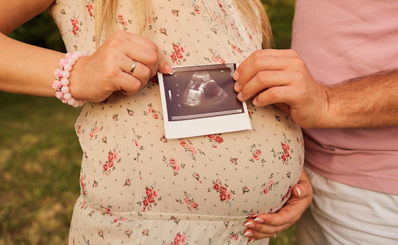 Couple holding ultrasound picture of woman's pregnant stomach