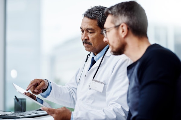 a male doctor speaking with a male patient, looking at a chart