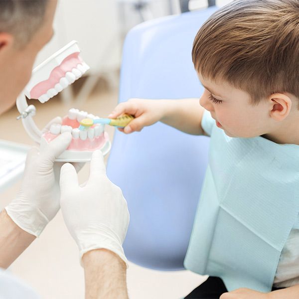 Dentist showing young boy how to brush model teeth