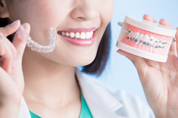 woman holding invisalign aligner and braces model