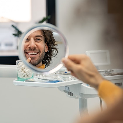 Dental patient looking in a hand mirror and smiling