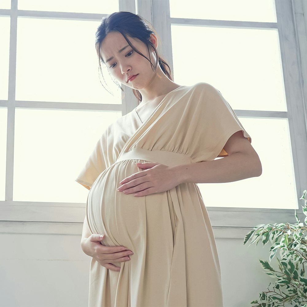 Young, pregnant, Asian woman looking worriedly at her stomach