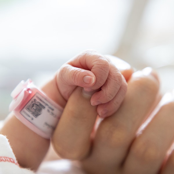 sleeping baby wearing hospital braclet clutching an adult's finger