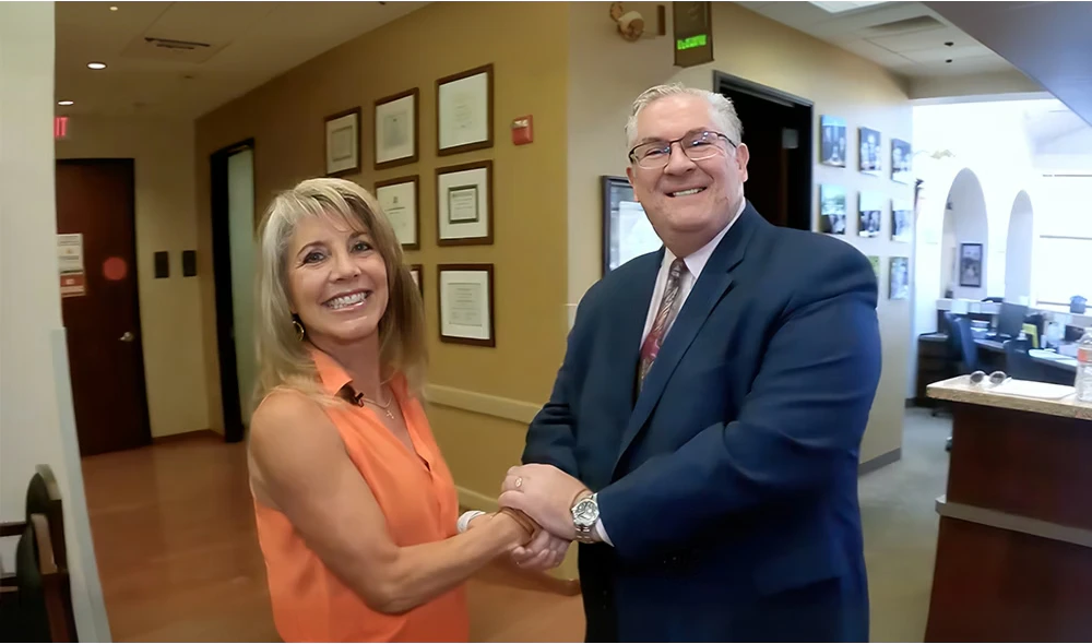 A smiling patient shaking hands with Dr. Justo in the Arizona Eye Institute office hallway