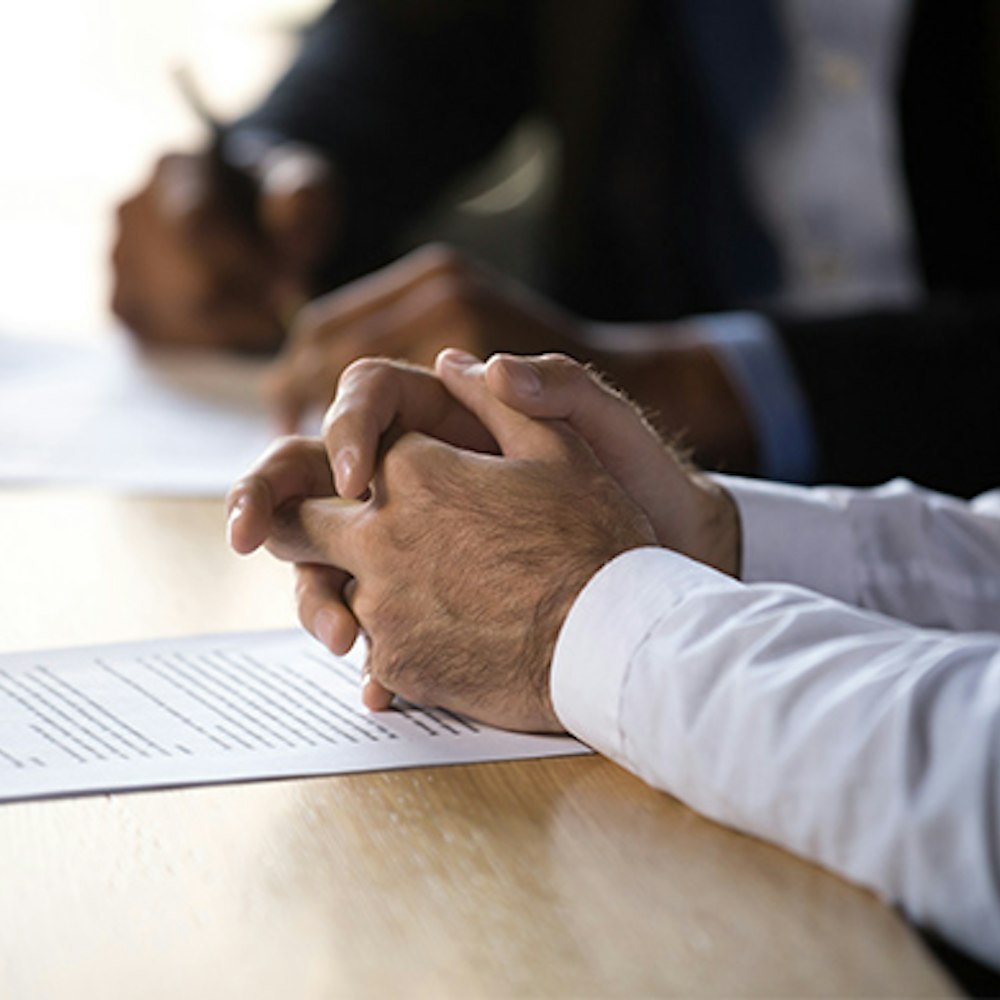 Person with clasped hands sitting at a desk with documents during a meeting
