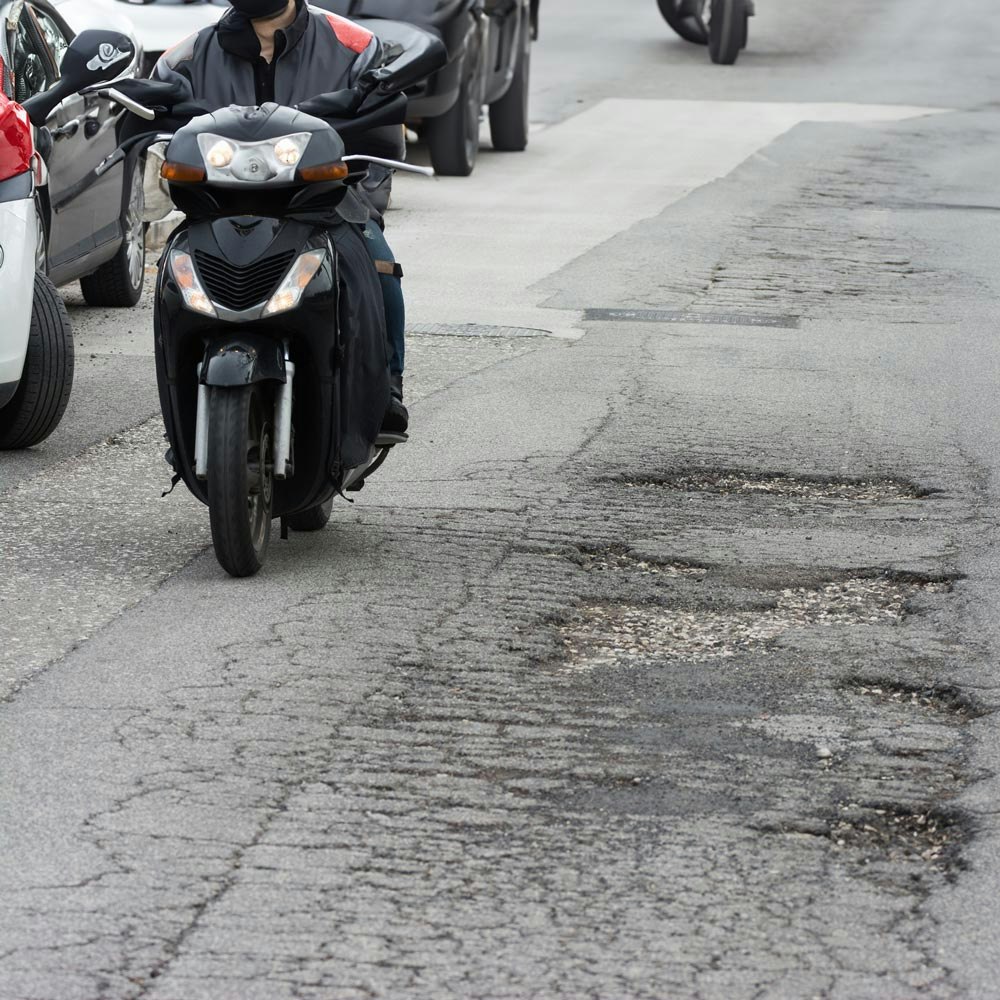 Motorcyclist and cars next to pot holes