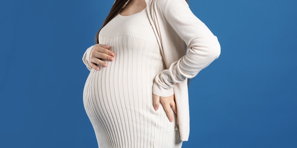 Pregnant woman wearing white dress and touching belly