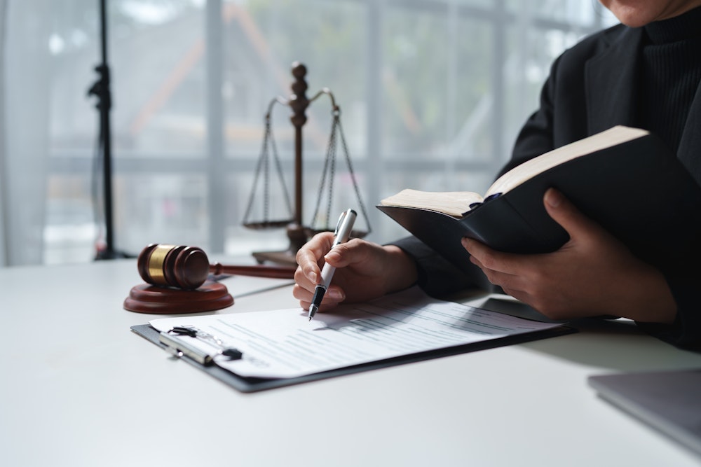 Close up of someone writing while looking at a legal book. Lady justice and a gavel in the background
