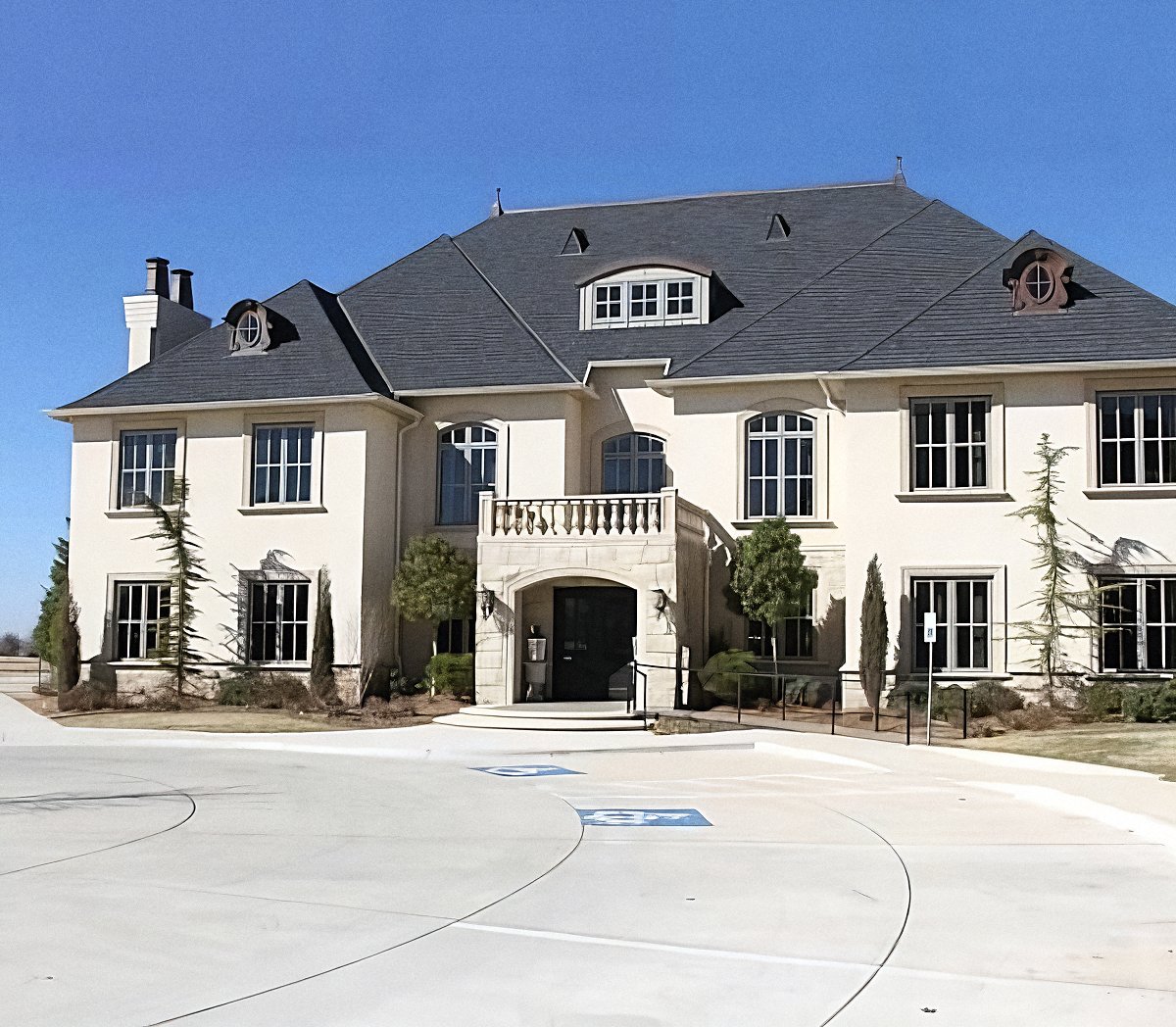Large two-story commercial building with light exterior walls, tall windows, and a wide entrance driveway