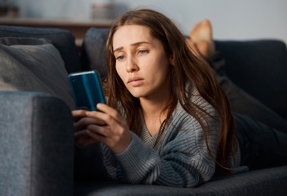 Woman lying on a couch looking at her phone with a concerned expression