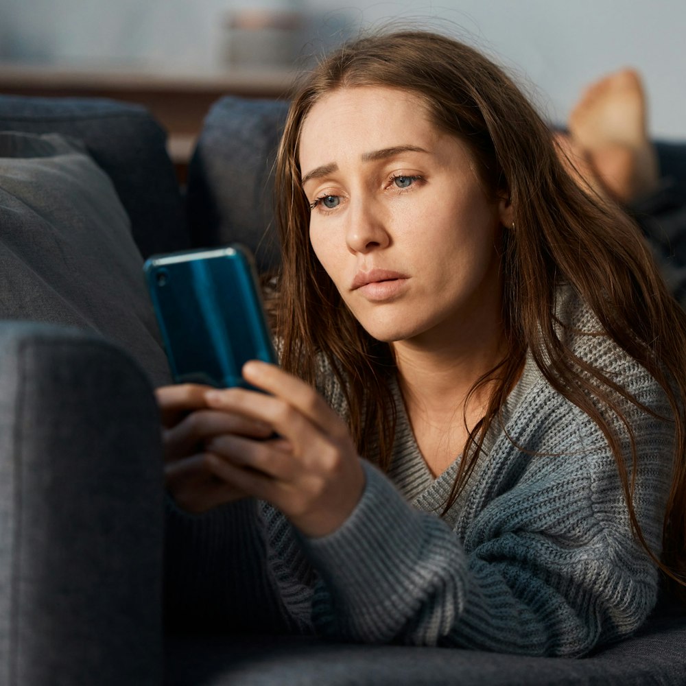 Woman lying on a couch looking at her phone with a concerned expression