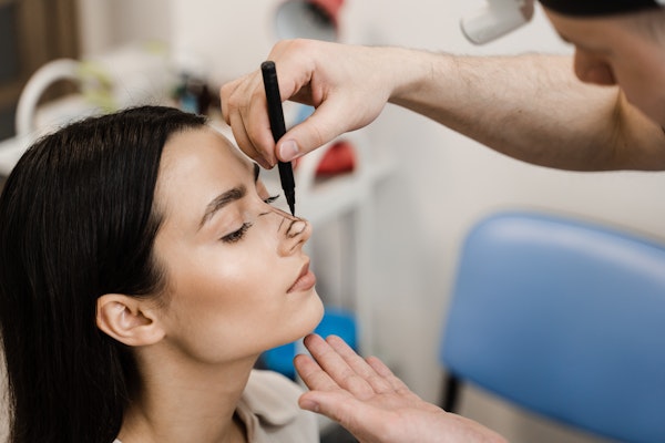 Plastic surgeon drawing on female patient's nose