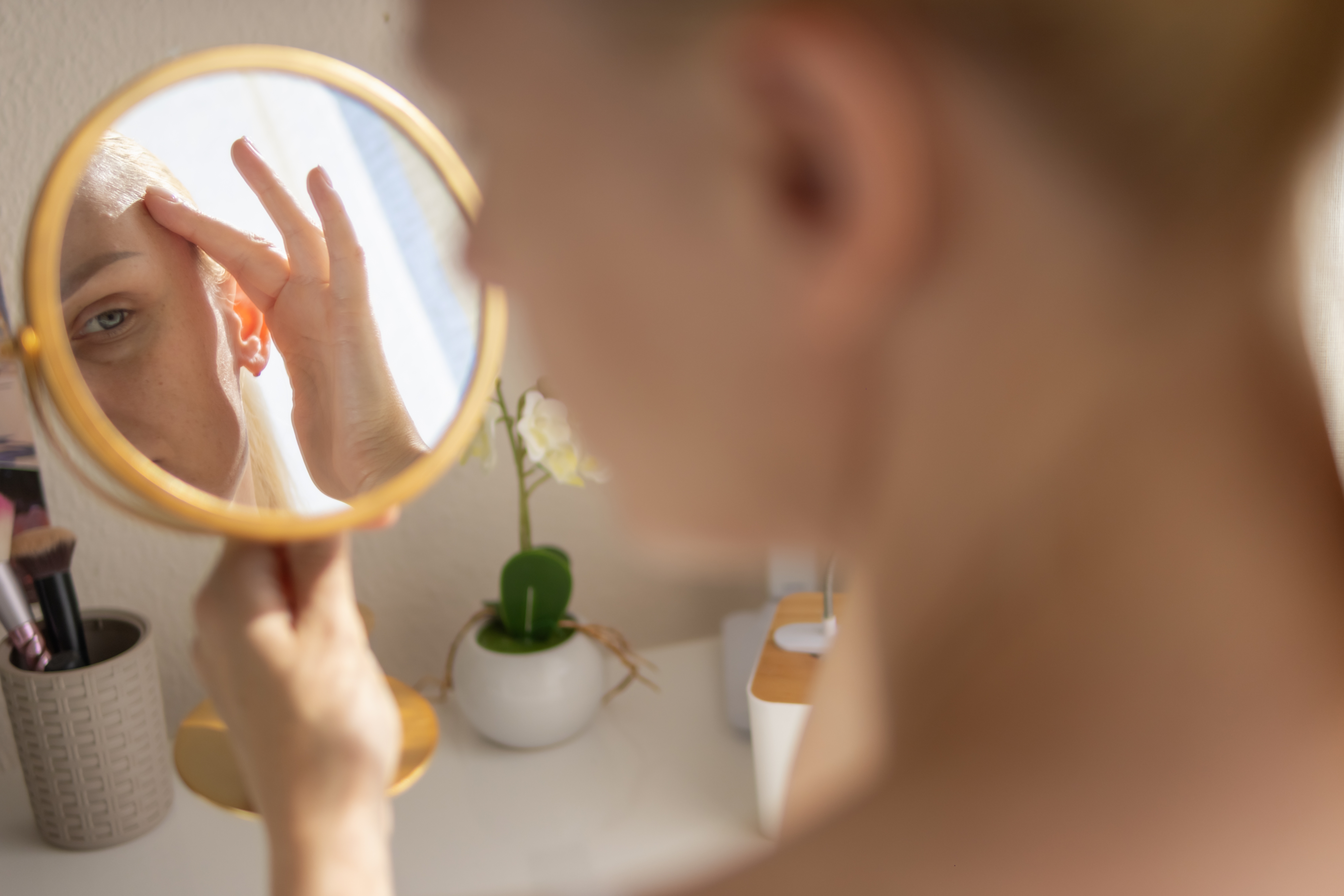 woman examining her eyelids in mirror