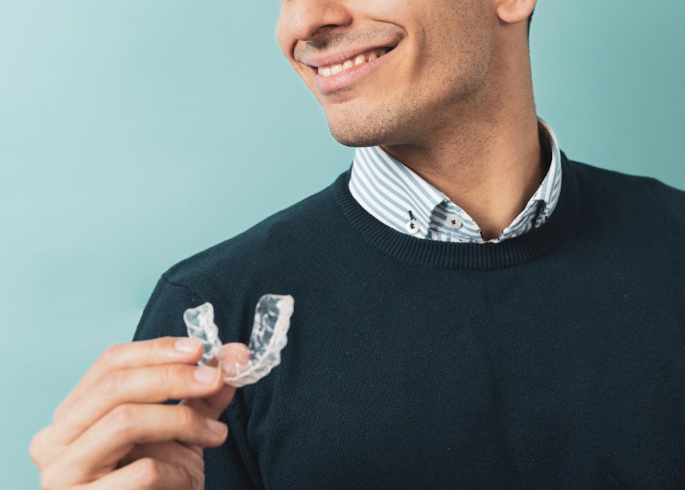 smiling anonymous man holding oral splint on a solid teal background
