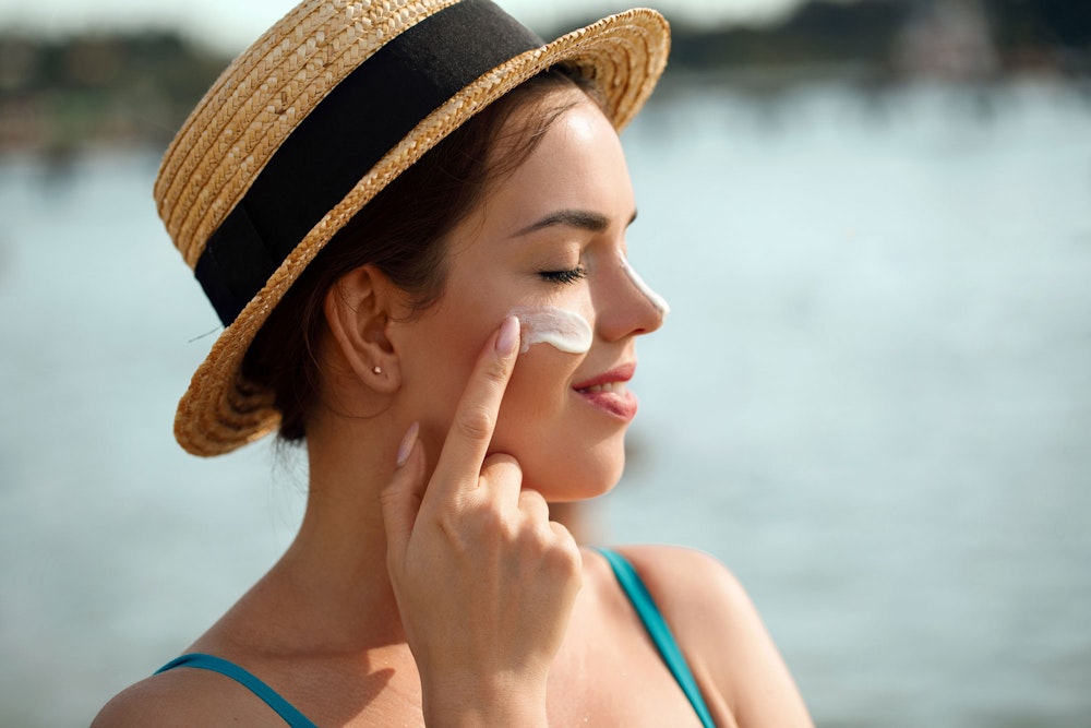 woman in straw hat applying sunscreen