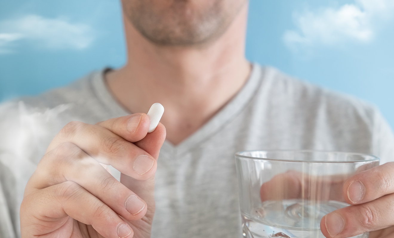 man holding pill and glass of water