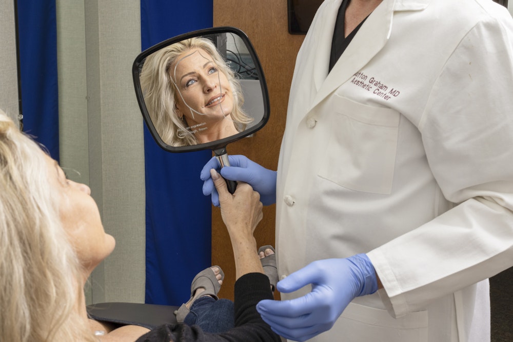 Happy woman meeting with Dr. Graham and looking in a hand mirror