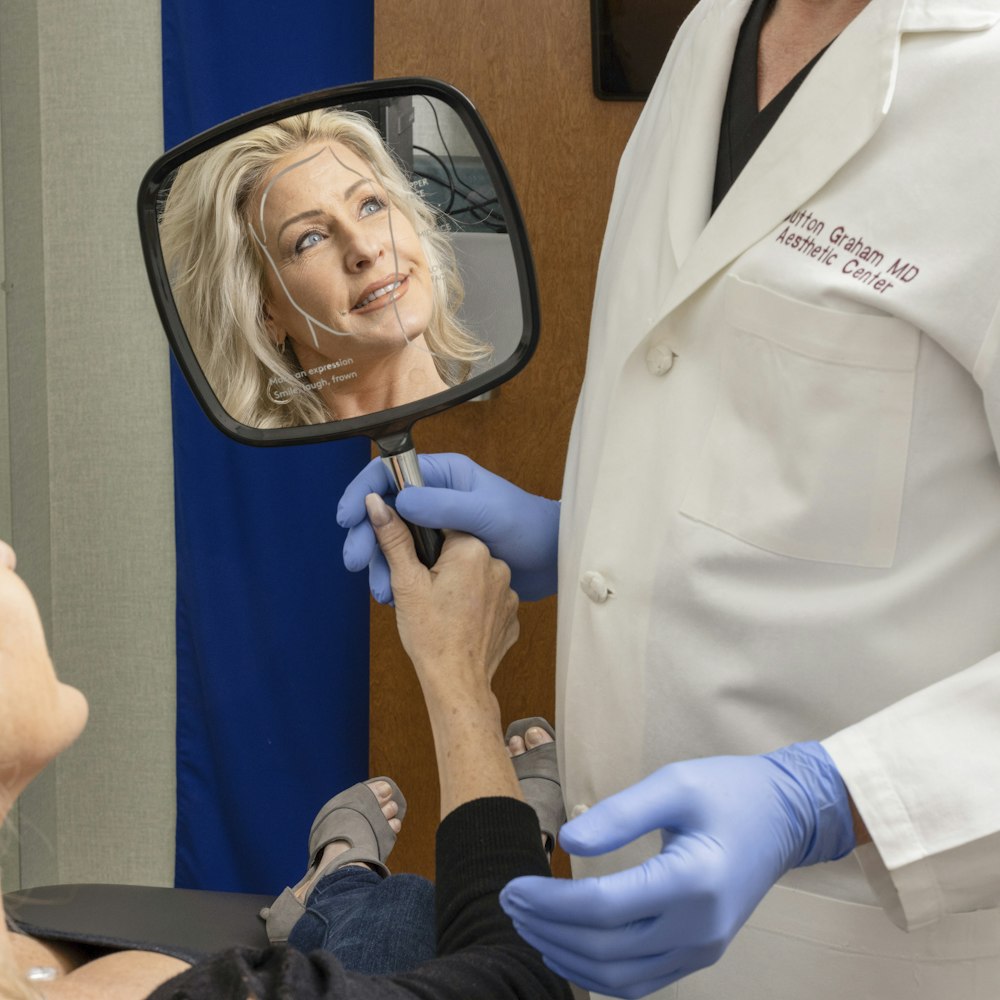 Happy woman meeting with Dr. Graham and looking in a hand mirror